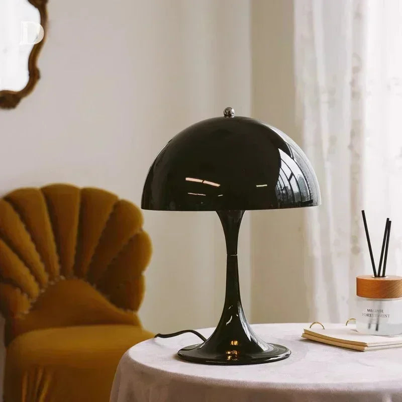 Black table lamp on a round table with a yellow chair and decorative items in the background.