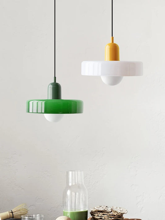 Two pendant lights, one green and one white with a yellow top, hanging against a light gray wall.