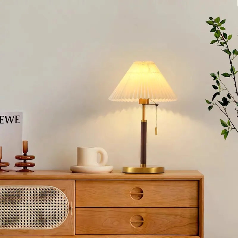 Table lamp on a wooden side table with a cup and decorative items, soft lighting.