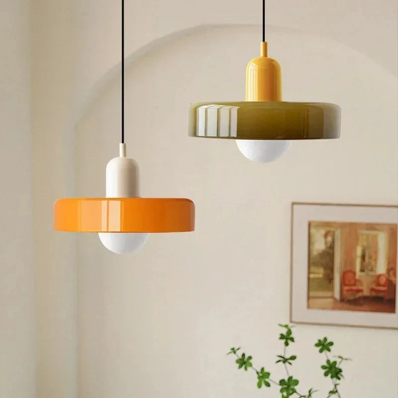 Two pendant lights, one orange and one green, hanging against a neutral wall with a framed picture.