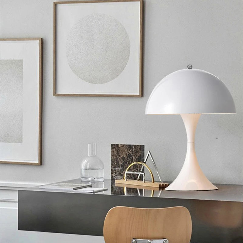 Modern office desk with a lamp, books, and decorative items against a gray wall.