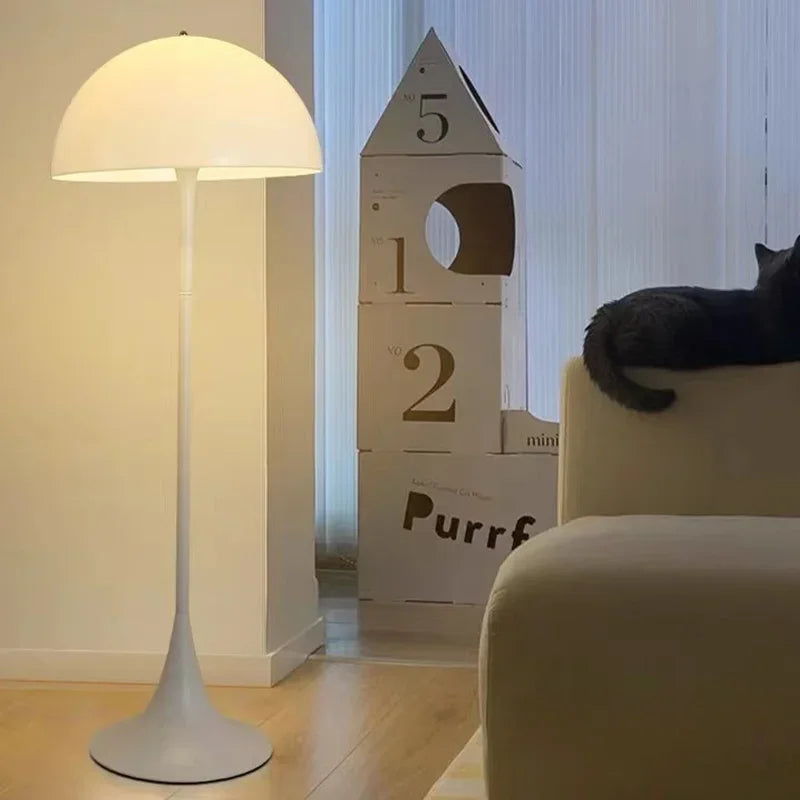 Cat sitting on a chair next to a lamp and a wooden cat house with numbers in a room.