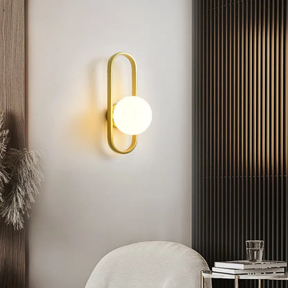 Modern wall lamp with gold fixture and white bulb on a neutral wall.
